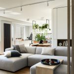 Stylish living room interior design with grey sofa, pouf and personal accessories. Dining space and kitchen on the background. Creative walls with woode pannels. Minimalistic style an plant love concept.