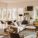 Wooden, round dining table in the corner of an open space living room interior with nordic furniture and decor